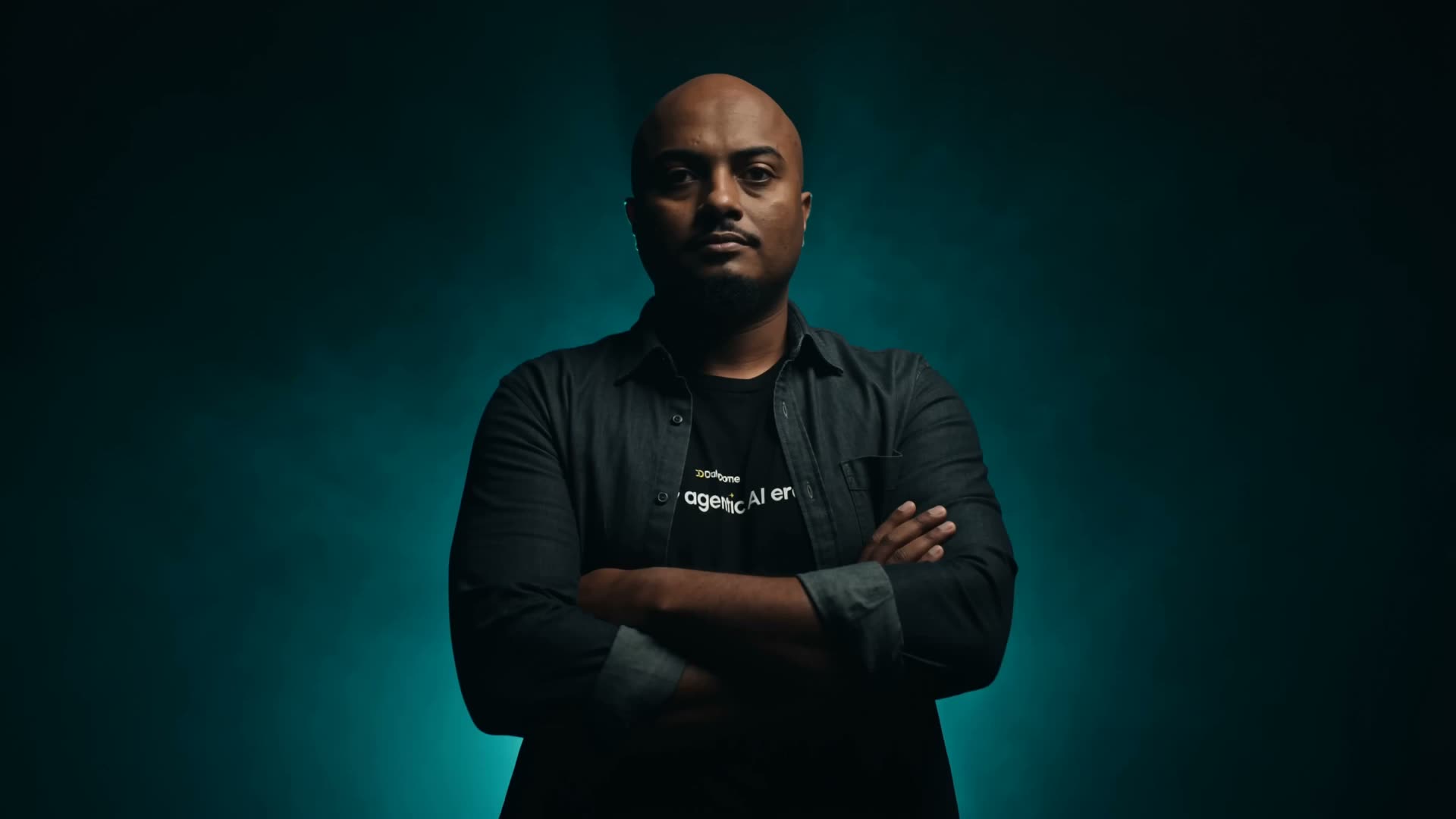 Travis Preudhomme standing arms crossed in a black studio with emerald rim lighting